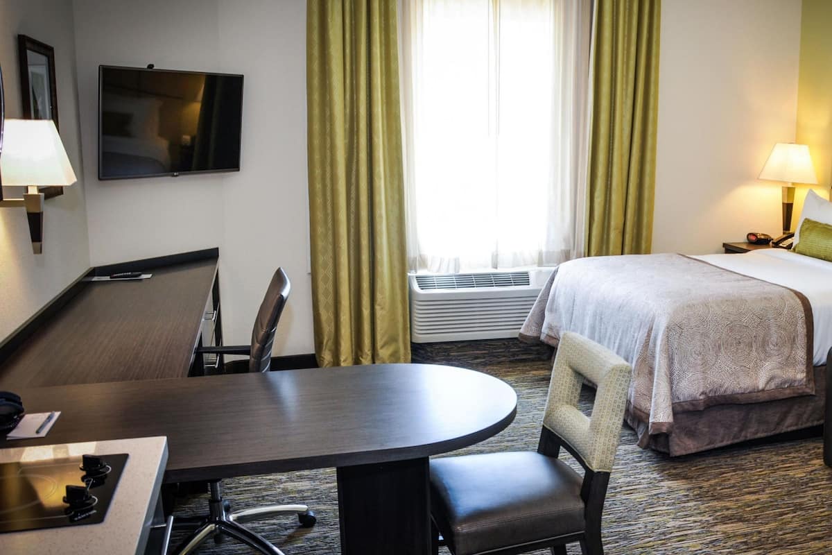 A hotel room with a bed, a desk with a chair, a TV, and a window with curtains.