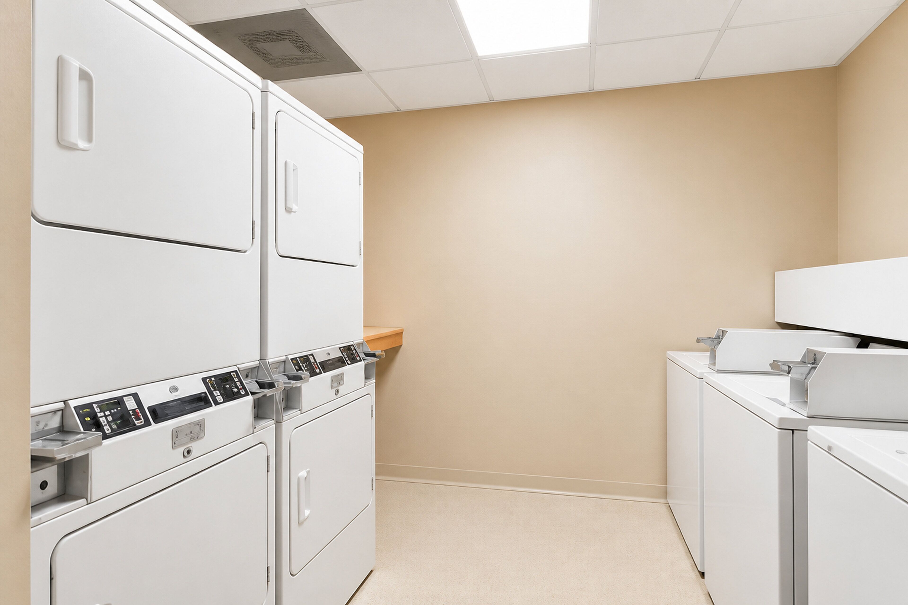 A laundry room with stacked washers and dryers, a wooden shelf, and a tiled floor.
