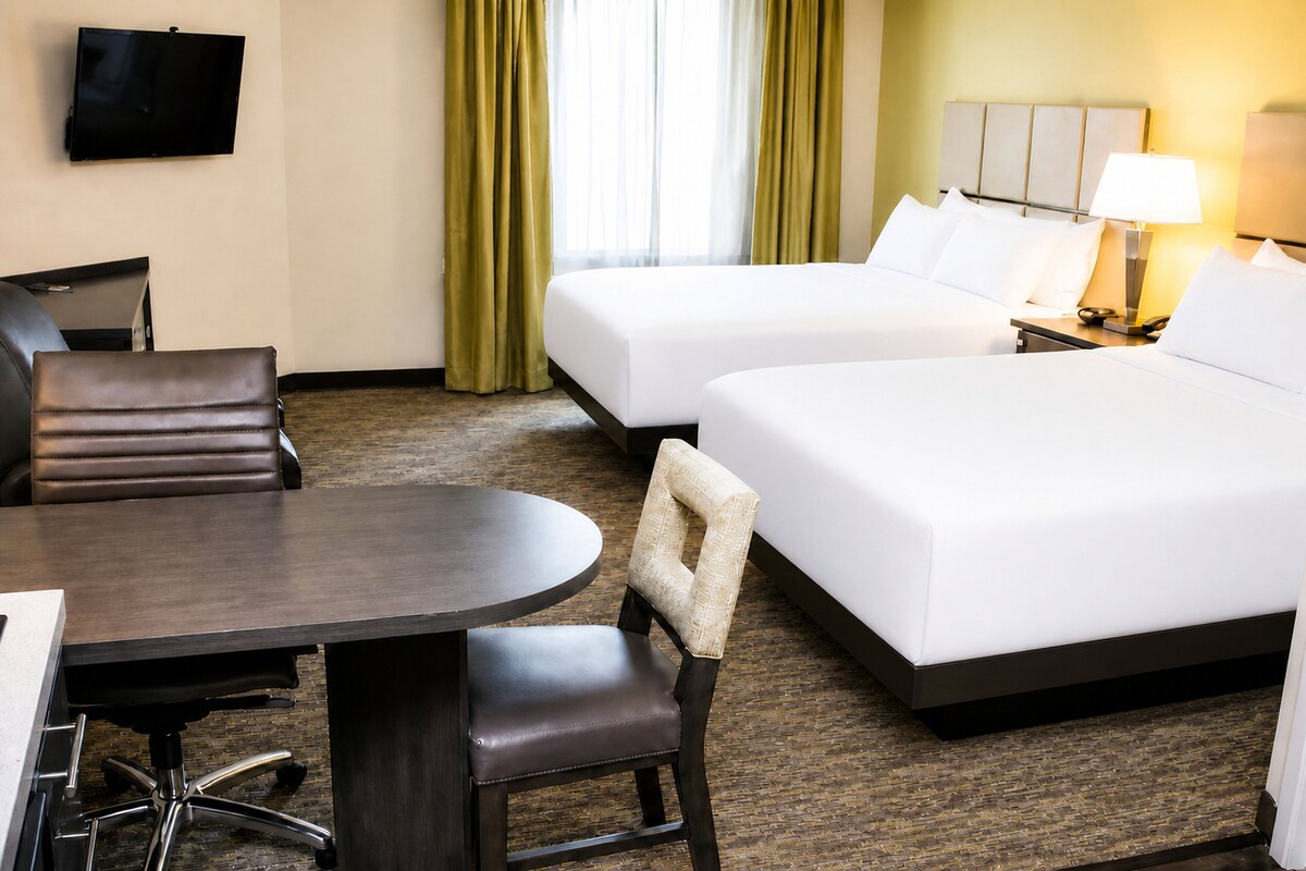 Een hotelkamer met een bureau, twee bedden, een stoel, een televisie en een lamp.