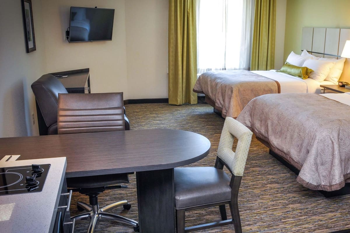 A hotel room with two beds, a desk with a chair, a television, and a window with curtains.