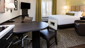 Quarto de hotel com cama, escrivaninha, cadeira, televisão e janela com cortinas.