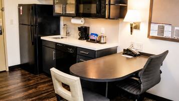 Cocina compacta con refrigerador, microondas, cafetera y una pequeña mesa de comedor con sillas.