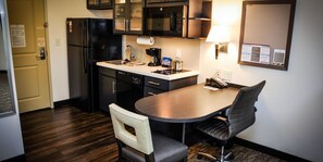 Una cocina compacta con refrigerador, microondas y cafetera. Cuenta con una mesa de comedor con dos sillas y una lámpara.