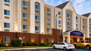 A hotel building with multiple windows, a sign for 'Candlewood Suites', and a parking area with cars. - Candlewood Suites Pearl by IHG (Pearl)