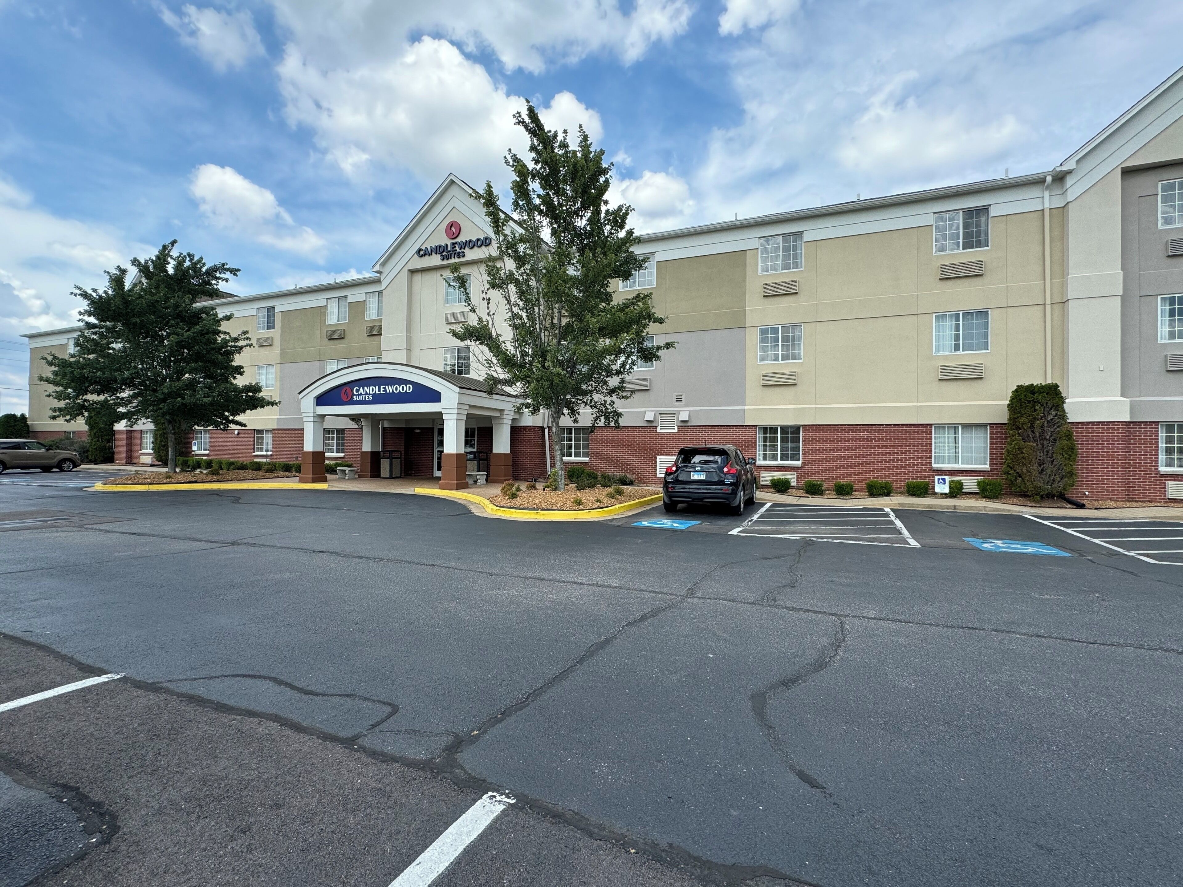 A hotel with a prominent entrance, parking lot, and a clear sky.