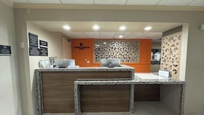 Ein Empfangsschalter mit Holzoptik und zwei Laptops darauf. Ein Schild mit der Aufschrift 'Candlewood Suites' und eine Wand mit einem geometrischen Muster.
