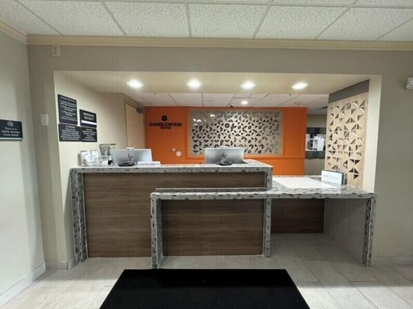 A reception desk with a wooden finish and two laptops on it. There is a sign that reads "Candlewood Suites" and a decorative wall with a geometric pattern. - Candlewood Suites Olive Branch by IHG (Olive Branch)