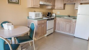 A small kitchenette with a microwave, stove, and sink. There is a table with two chairs and a framed picture on the wall.