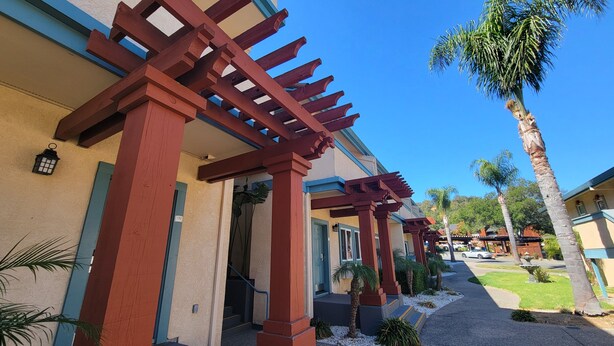 A building with a covered walkway, palm trees, and a clear blue sky.