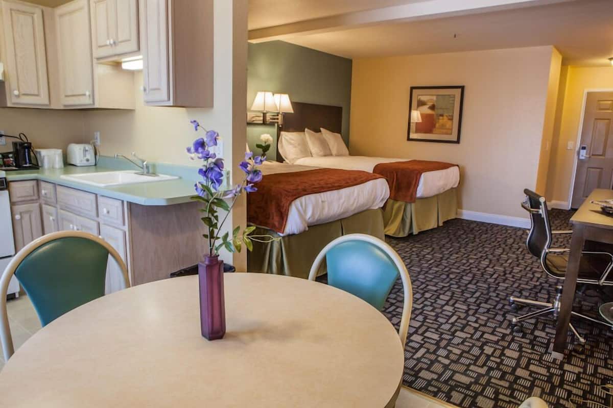 A hotel room with a kitchenette, two beds, a dining table, and chairs.