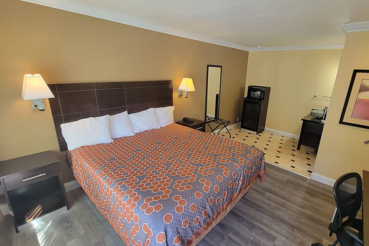 A hotel room with a large bed, two bedside lamps, a flat-screen TV, a small desk, a chair, and a framed picture on the wall.