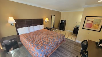 Ett hotellrum med en stor säng, två sänglampor, en platt-TV, ett litet skrivbord, en stol och en inramad tavla på väggen.