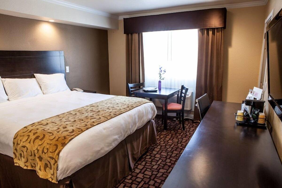 A hotel room with a large bed, a desk, a chair, and a window with curtains.