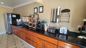 A hotel kitchen with a refrigerator, coffee machine, and various food items on the counter.
