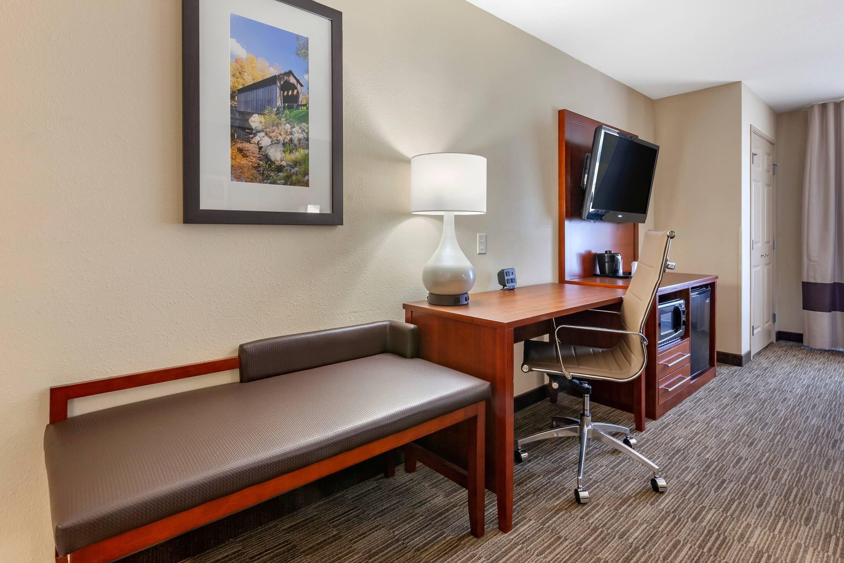 Une chambre d’hôtel avec un lit, un bureau et une chaise, une télévision et un tableau encadré au mur.