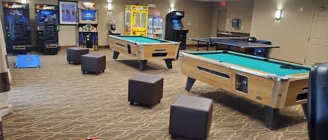 A pool table area with multiple tables and a dartboard, surrounded by arcade games and a carpeted floor.