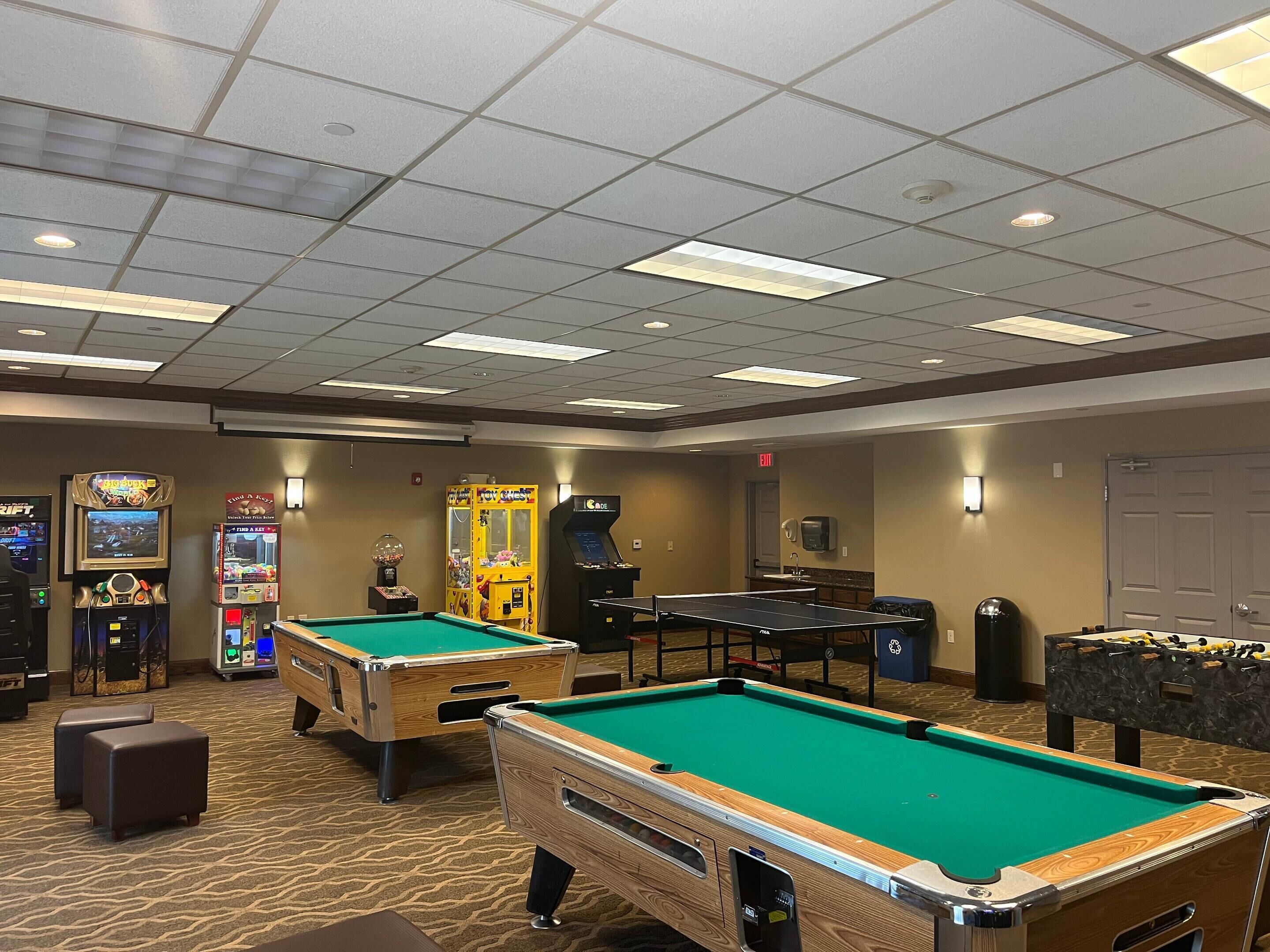 A pool table, two foosball tables, and various arcade games in a room with patterned carpet and recessed lighting.