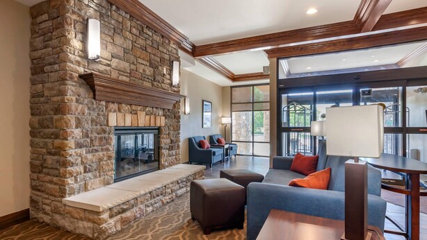 A stone fireplace, a blue sofa, a wooden table, and a patterned carpet in a room with large windows. - Comfort Suites Oshkosh West (Oshkosh)