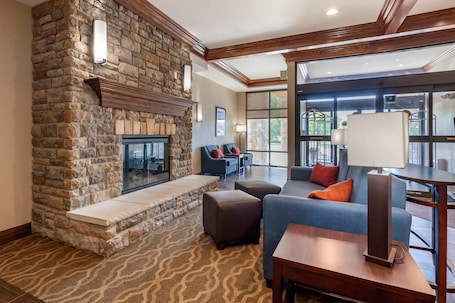 A stone fireplace, a blue sofa, a wooden table, and a patterned carpet in a room with large windows.