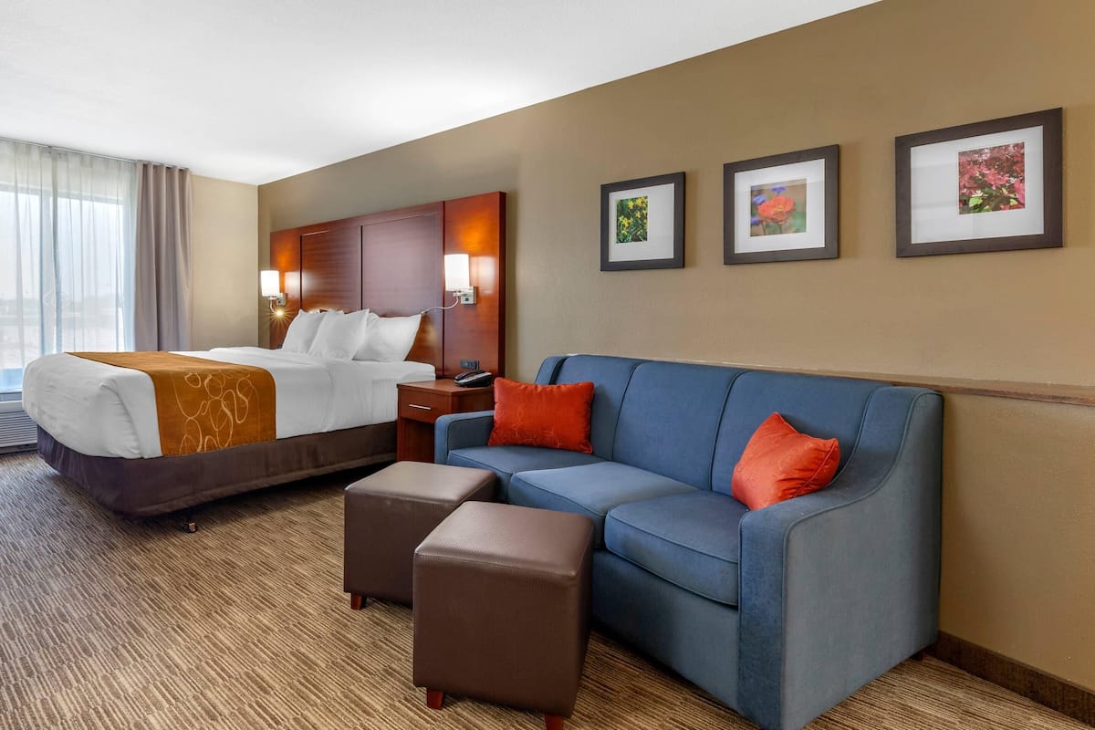 A hotel room with a bed, a sofa, a coffee table, and framed pictures on the wall.