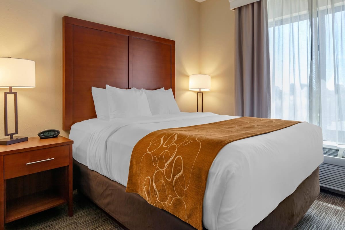 A hotel room with a large bed, two bedside lamps, a nightstand, and a window with curtains.