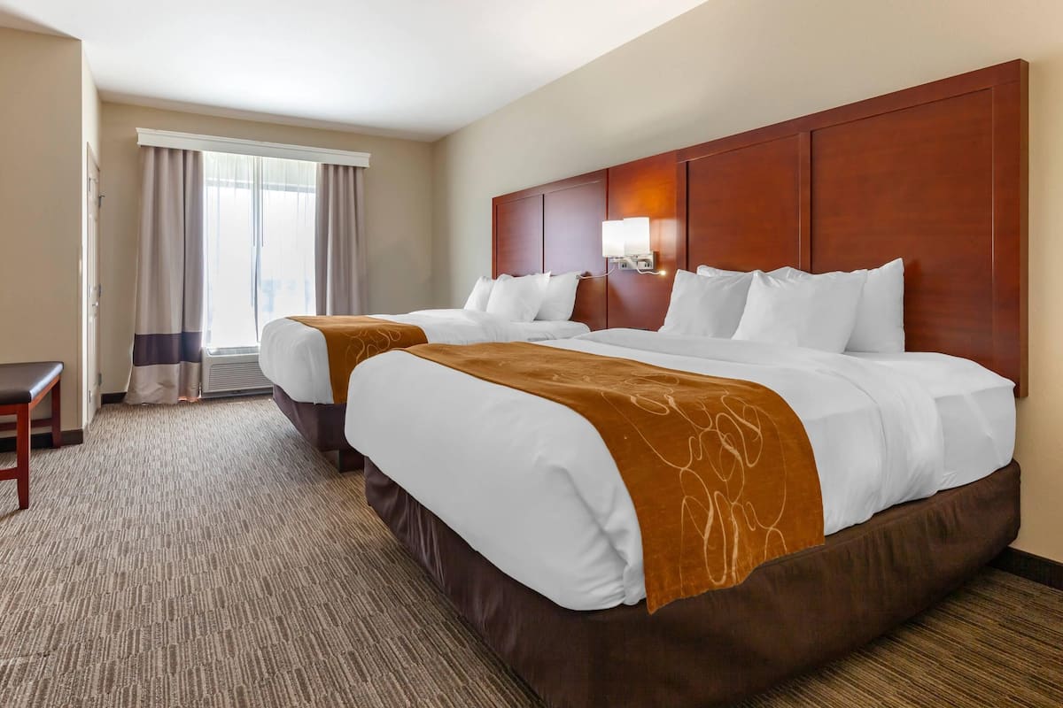 A hotel room with two beds, a desk, and a large window with curtains.