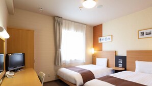 Une chambre d’hôtel avec deux lits, un bureau avec un ordinateur, une chaise et une fenêtre avec des rideaux.
