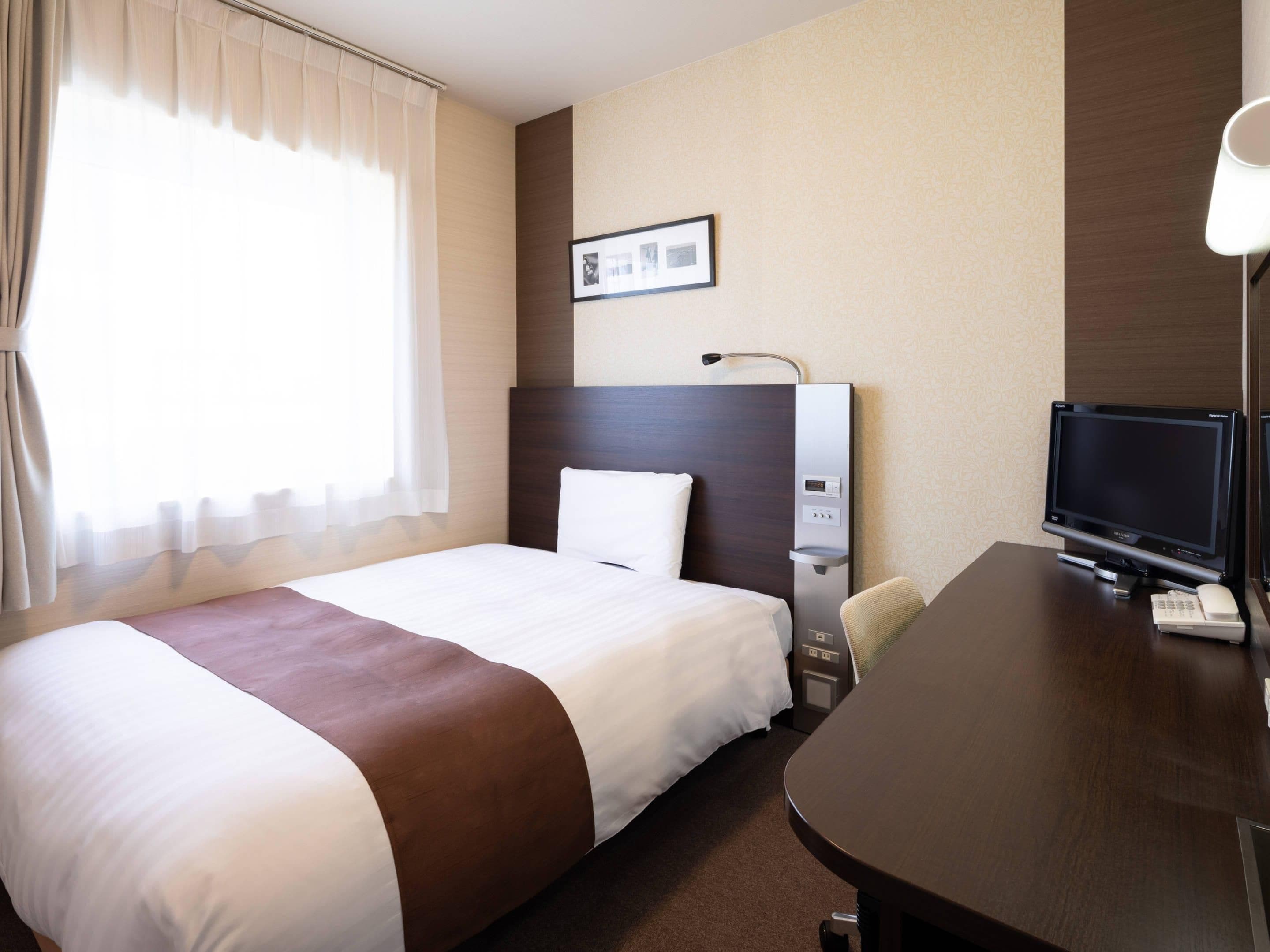 Ein Hotelzimmer mit einem großen Bett, einem Schreibtisch mit Computer und Telefon, einem Fernseher und einem Bild an der Wand.