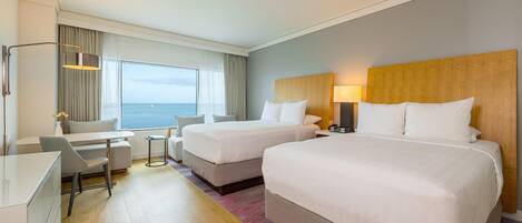 Une chambre d’hôtel avec deux lits, un bureau, une chaise, une lampe et une vue sur la mer.