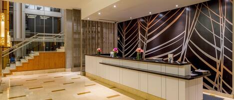 A modern hotel lobby with a reception desk, a staircase, and a decorative wall.