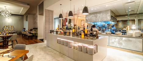 A modern restaurant with marble flooring, a central serving counter, and a kitchen area in the background.