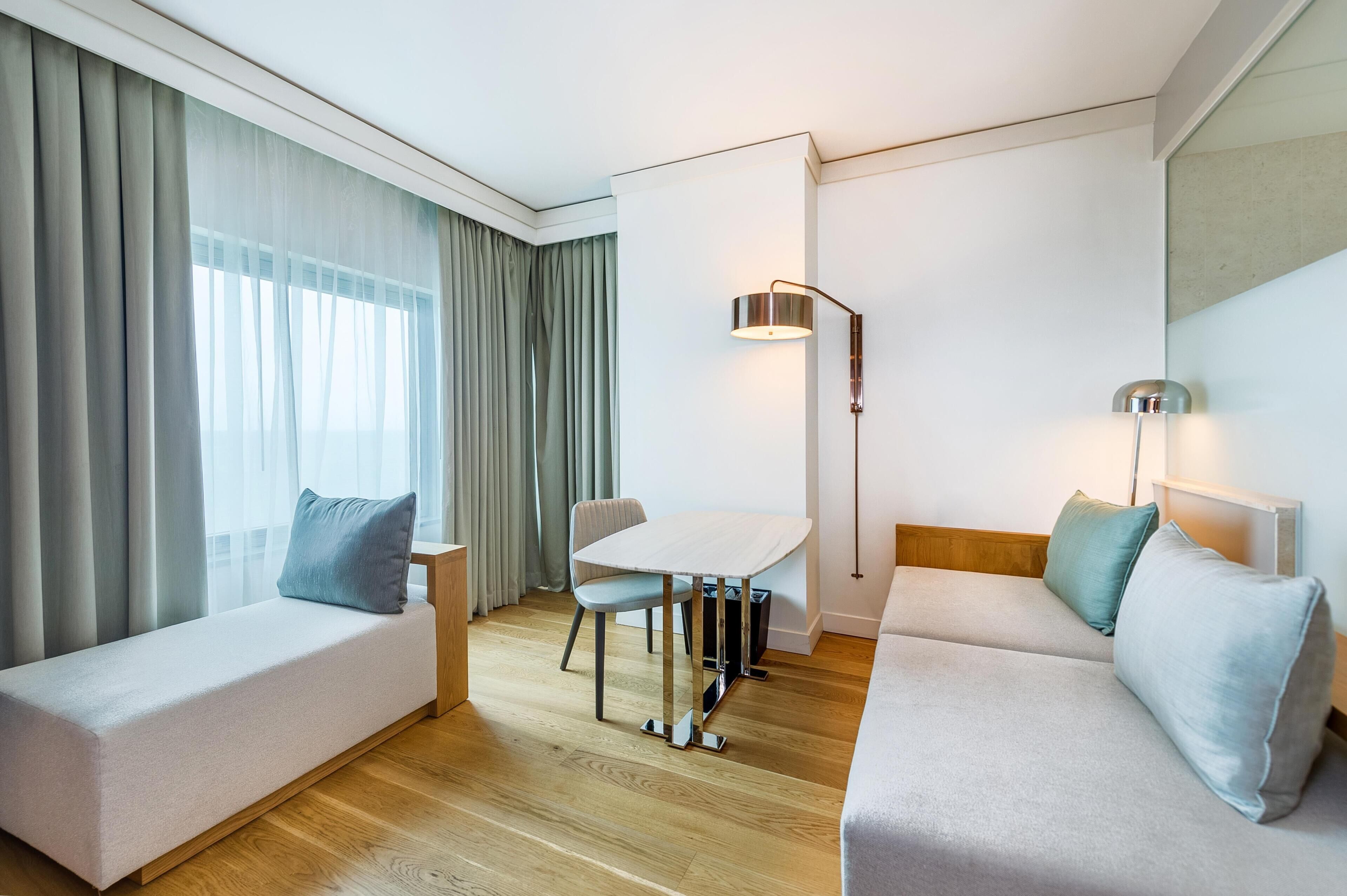 Quarto de hotel moderno com sofá, mesa pequena, cadeira e luminária.