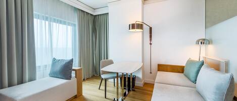 Quarto de hotel moderno com sofá, mesa pequena, cadeira e luminária.