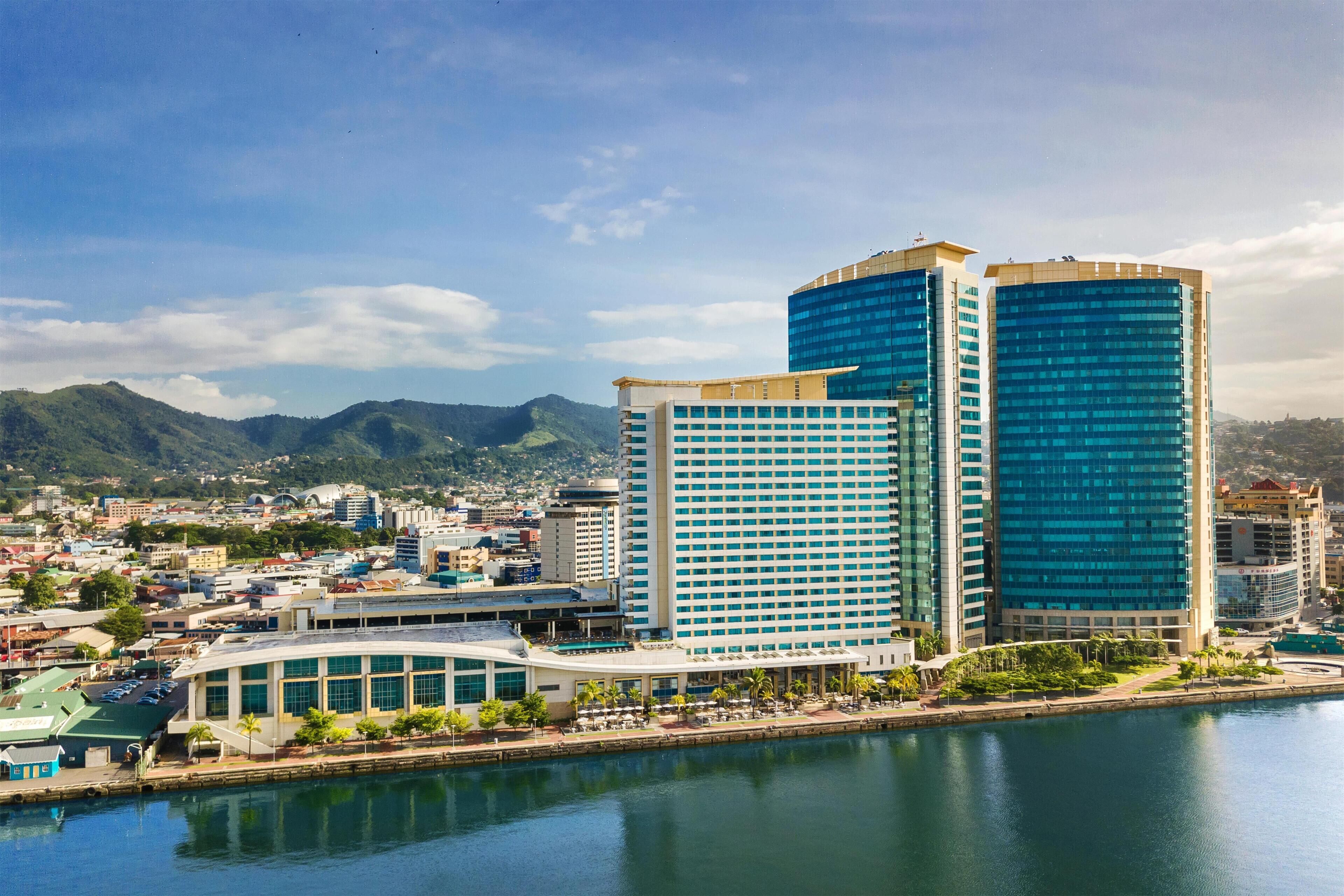 A cityscape with modern buildings, a waterfront, and a mountainous backdrop.