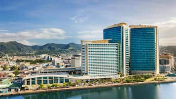 A cityscape with modern buildings, a waterfront, and a mountainous backdrop.
