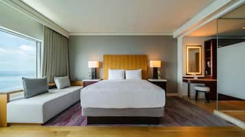 A hotel room with a large bed, a seating area, a desk, and a view of the ocean.
