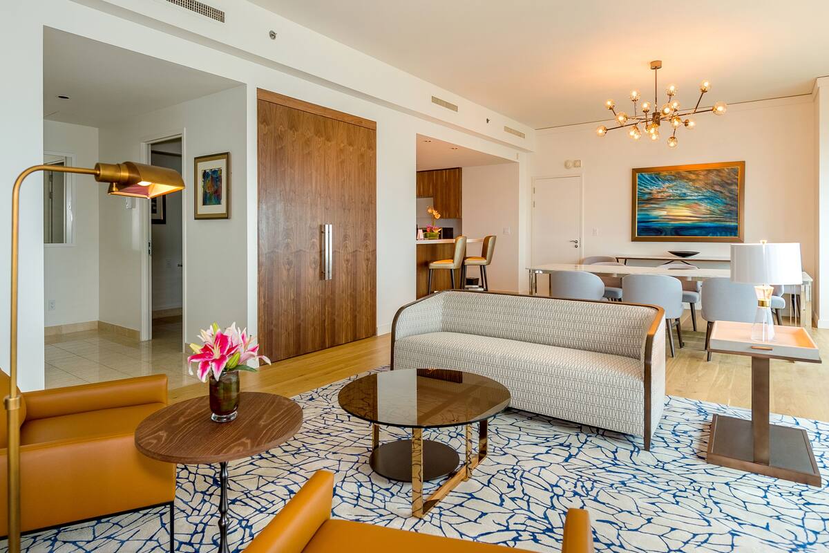 A modern hotel room with a sofa, a round table, a lamp, and a painting on the wall.