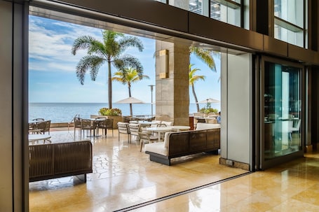 Ein Sitzbereich im Freien mit Tischen und Stühlen, Palmen und Blick auf das Meer.. Hyatt Regency Trinidad