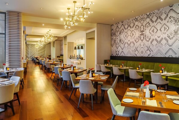Un restaurante con varias mesas, sillas y un muro con diseño.