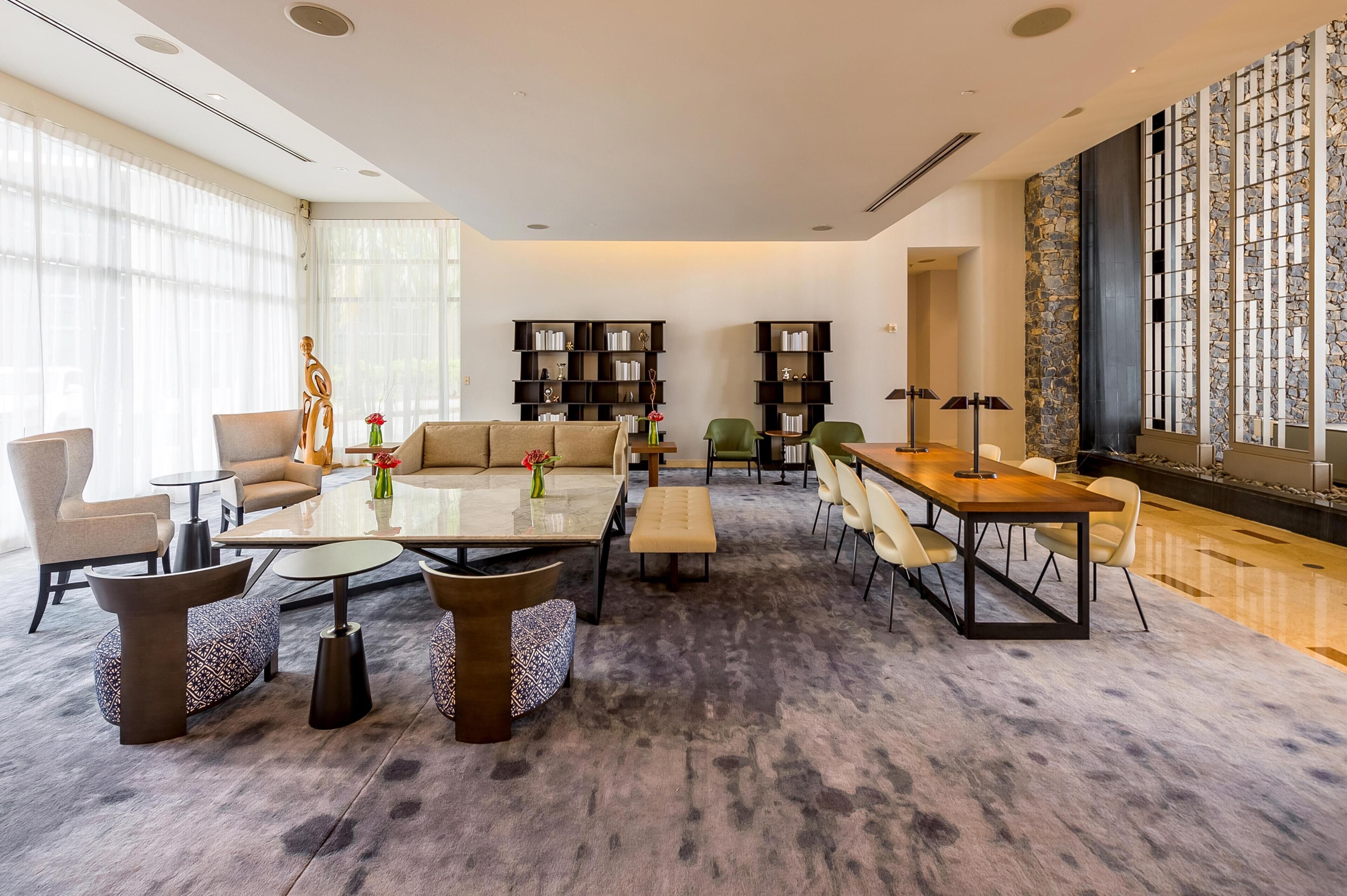 A modern living room with a sofa, coffee table, and chairs, a dining area with a table and chairs, and a bookshelf.