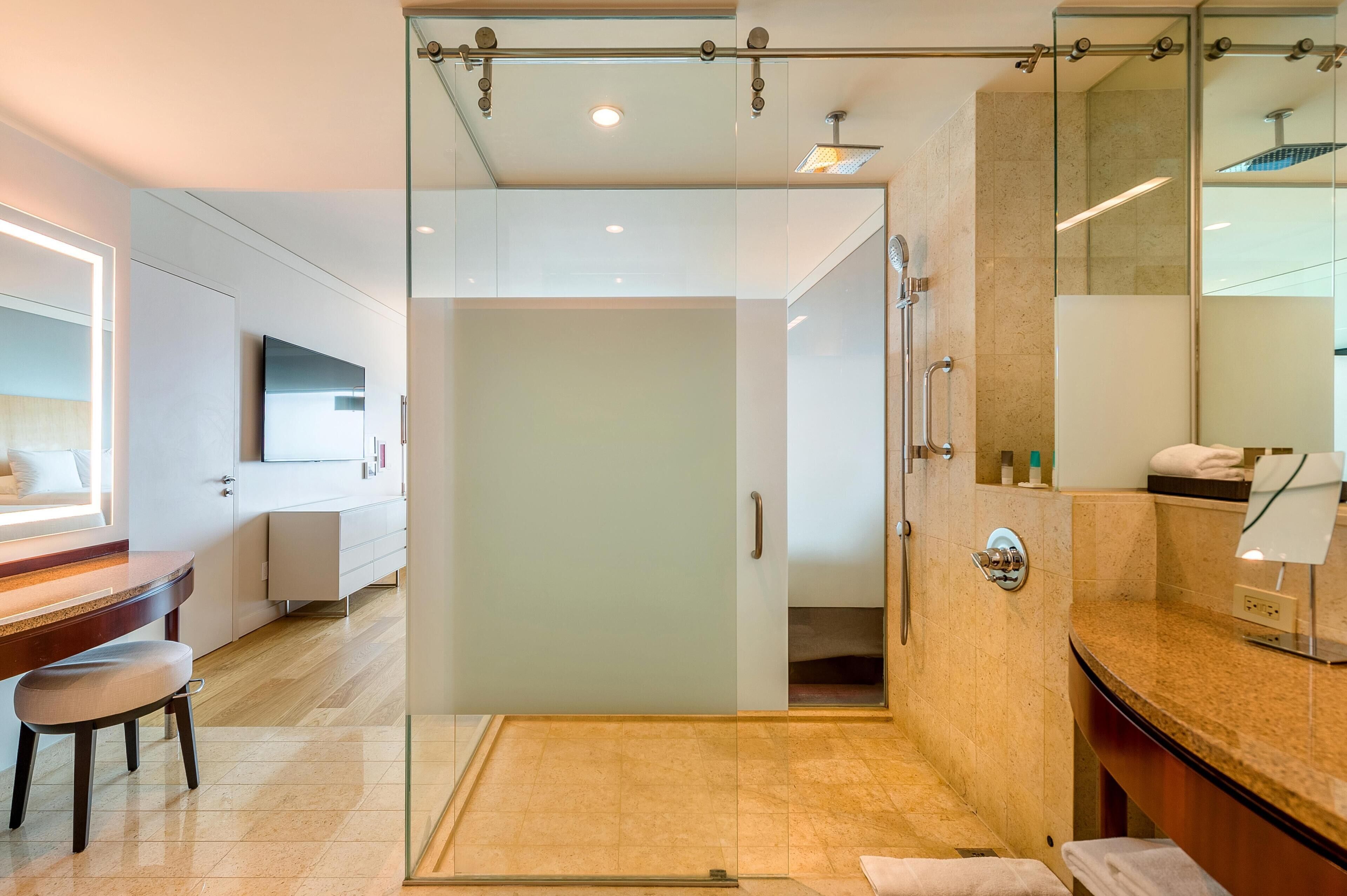 A modern bathroom with a glass shower enclosure, a vanity with a mirror, and a wooden desk with a chair.