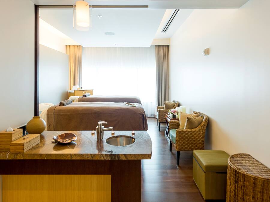A hotel room with a large bed, a sitting area with a chair, a small table, and a vanity with a sink.