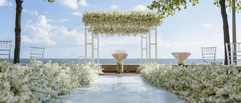 A wedding aisle with white floral decorations and a view of the sea.