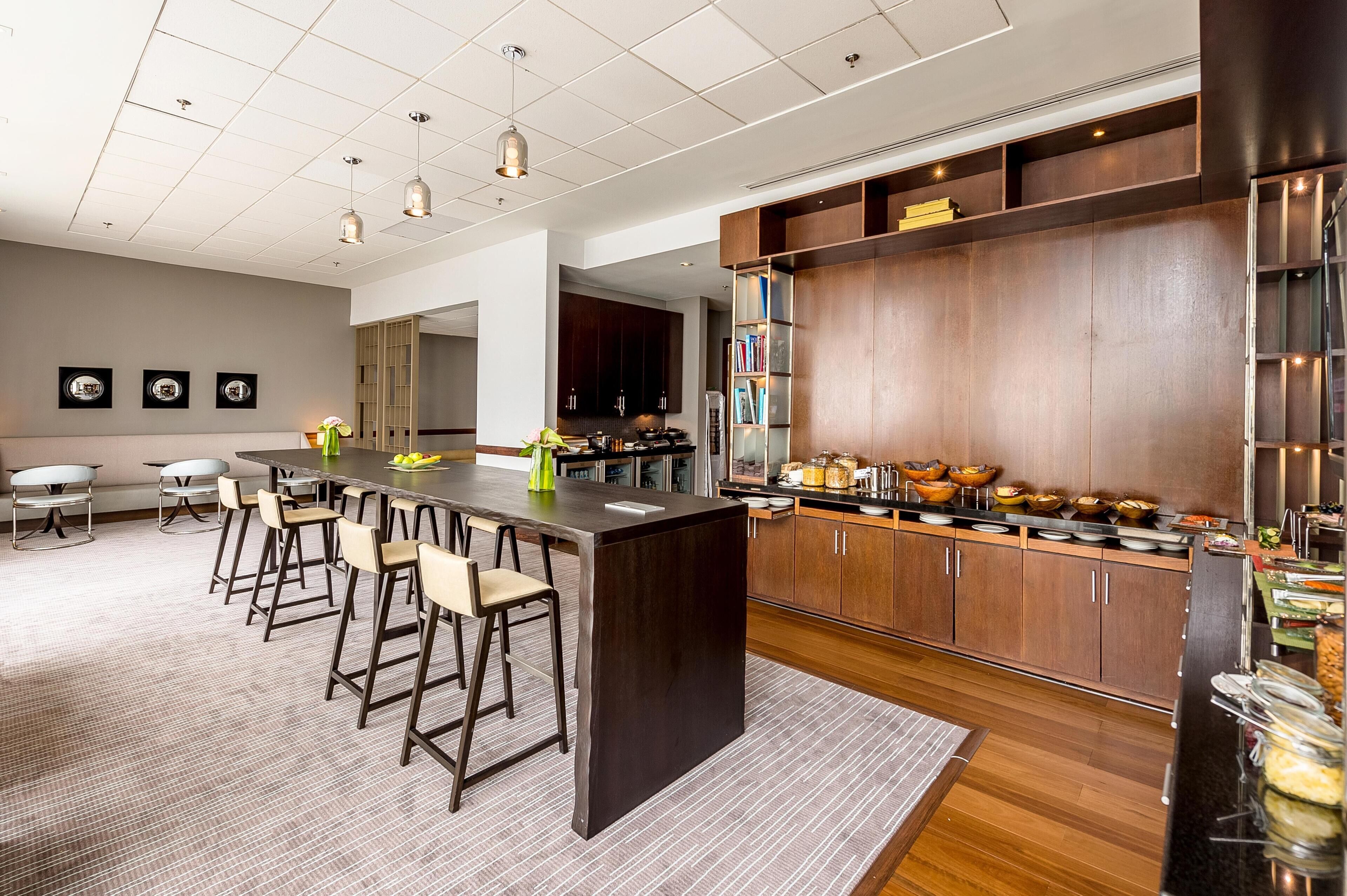 Una cocina moderna con una isla central, taburetes de bar, armarios de madera y una zona de buffet.