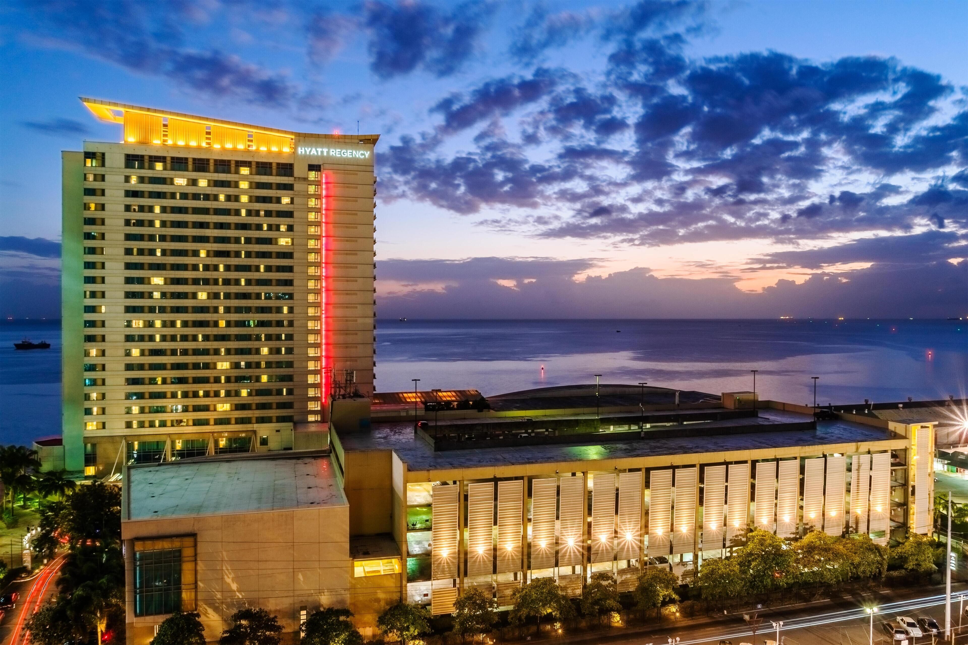 A high-rise hotel with a prominent 'Hyatt Regency' sign, a waterfront view, and a modern architectural design.
