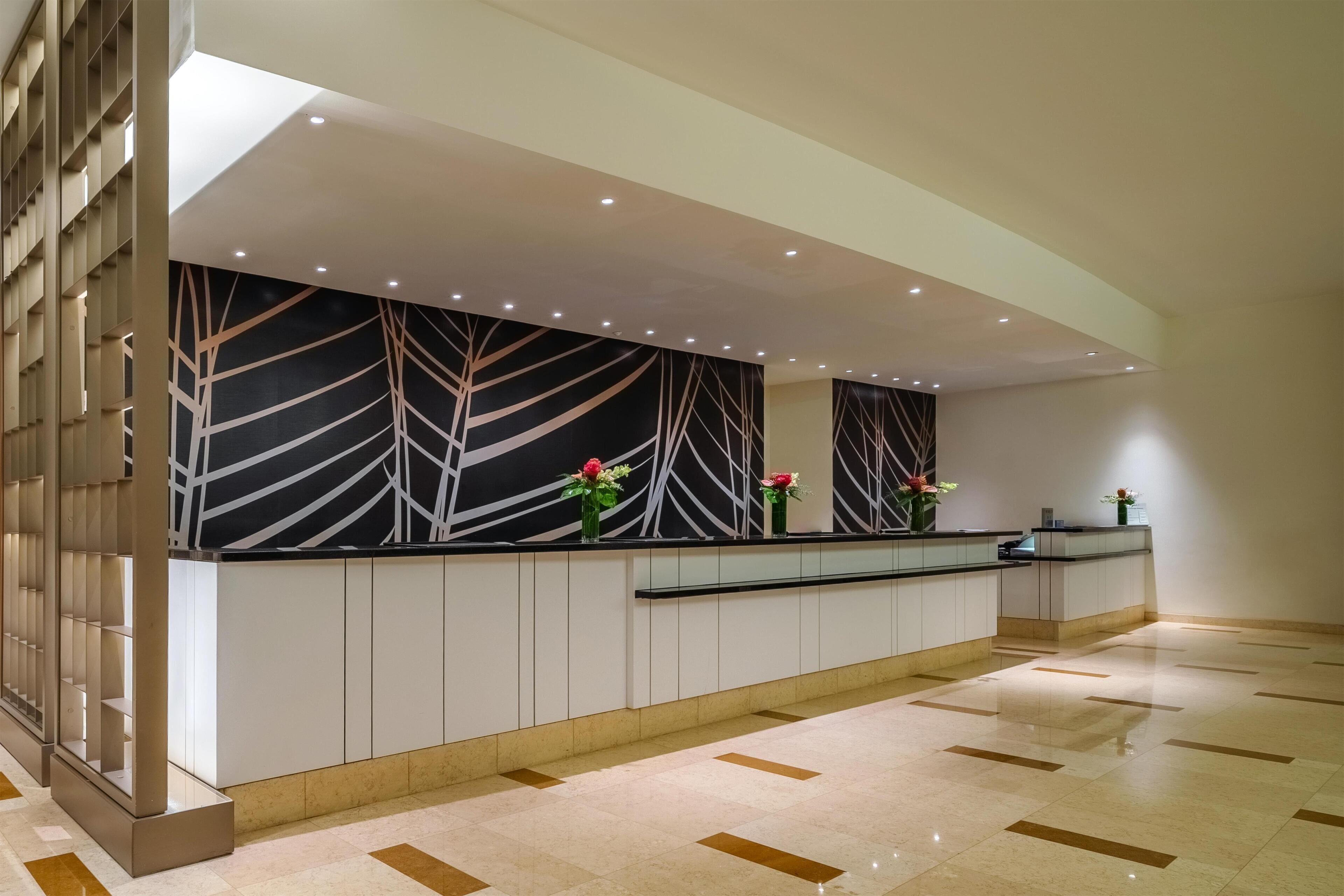 Un área de recepción con diseño moderno, que incluye un mostrador de recepción, una pared decorativa con patrones abstractos y un suelo de baldosas.