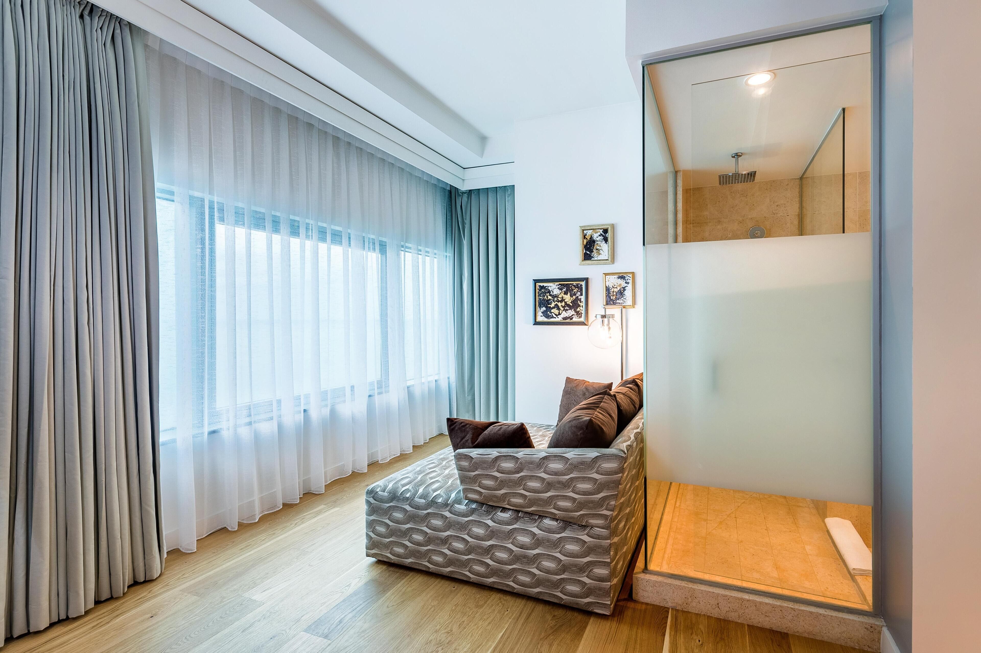 A modern bedroom with a bed, curtains, a bedside table, a mirror, and framed pictures on the wall.