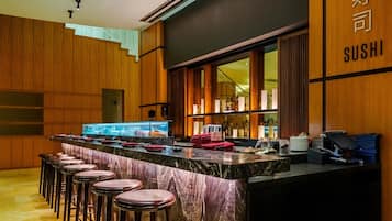 Un bar de sushi con mostrador de mármol, taburetes y una caja registradora.