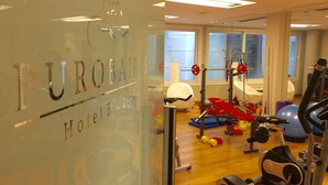 Een sportschool met diverse fitnessapparaten, waaronder een loopband, een hometrainer en krachtapparaten.