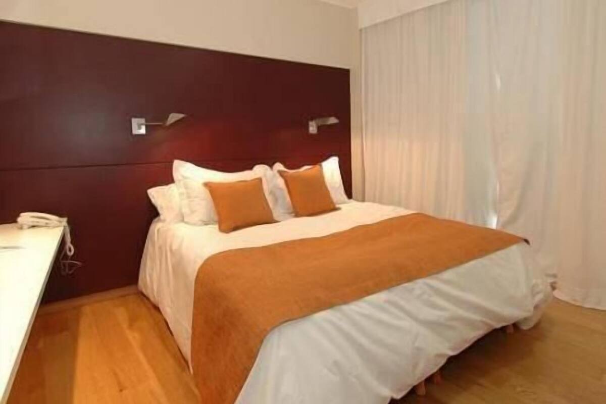 Une chambre d’hôtel avec un lit, une table de chevet et une fenêtre avec des rideaux.